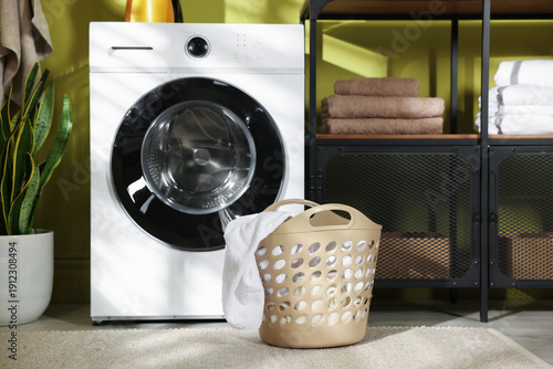Laundry basket with clothes and washing machine indoors