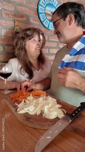 Senior couple cooking, drinking wine, and kissing in the kitchen