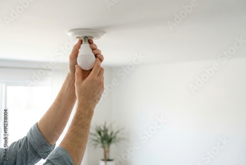 A person's hands screw a new energy-efficient LED light bulb into a white ceiling light fixture.