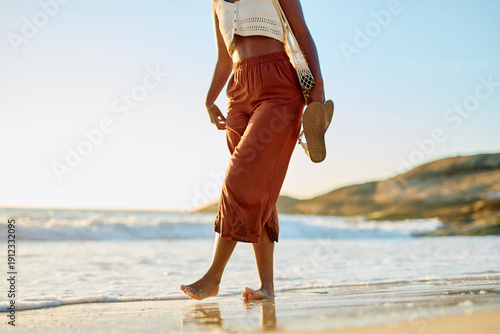 Fotografía Woman feeling ocean waves on her bare feet, carrying sandals while strolling alo
