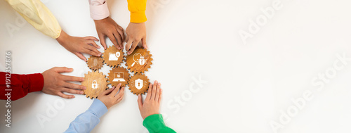 Fotografi Diverse hands gather around gears with icons depicting cybersecurity themes, showcasing the importance of collaboration in enhancing digital security and awareness