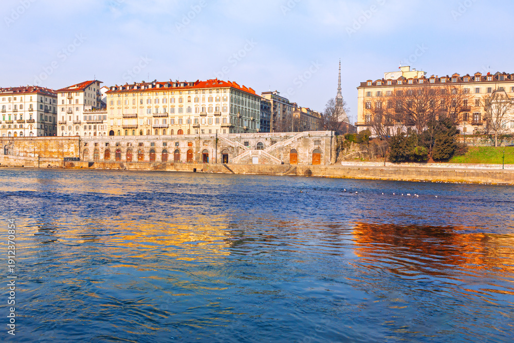Fototapeta premium Murazzi del Po embankment along the Po River in Turin, Italy. Historic area features stone arches reflecting on the water beneath the iconic Mole Antonelliana tower