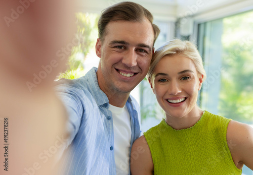 Couple smiling posing at home in blue shirt, green top holding smartphone by windows, plant visible