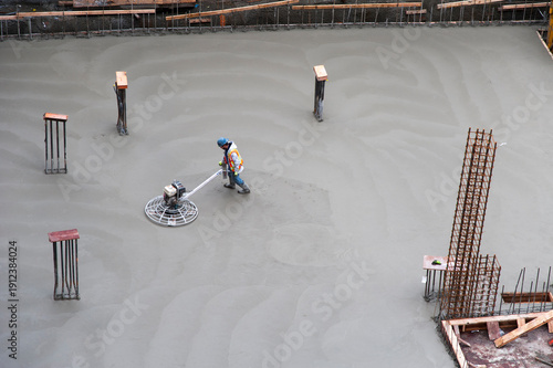 Canada, BC, Vancouver.  Construction worker using a power trowel to smooth the surface of concrete slab floor in building foundation.
