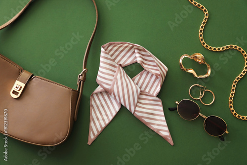 Stylish handkerchief, bag and other accessories on dark green background, flat lay