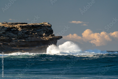 Dramatic waves smash against towering sandstone cliffs at dusk