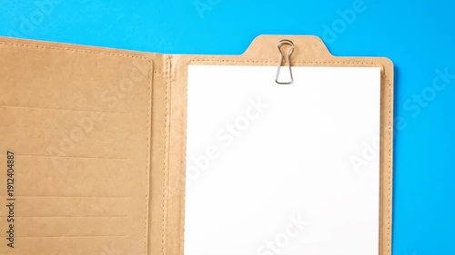 Open manila folder with blank white paper and binder clip on bright blue background