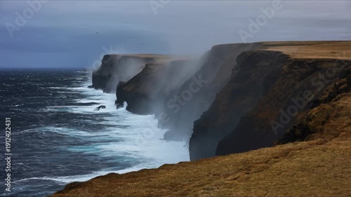 Dramatic ocean waves crash against rugged sea cliffs shrouded in mist on overcast day dramatic coastal erosion