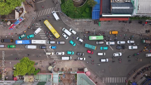 Top-down drone view of dense traffic at busy urban intersection in Ho Chi Minh City. Cars, buses and motorbikes create organized chaos typical of fast-growing Southeast Asian cities.