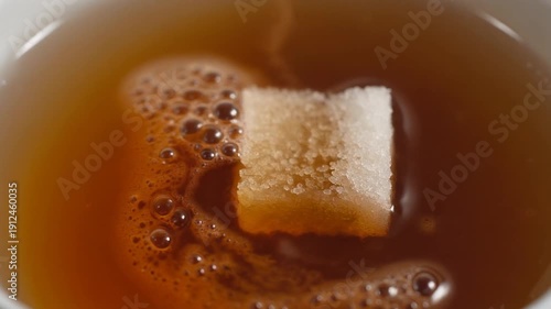 Sugar cube dissolving in hot tea, close-up, top view, sweetening beverage, morning drink.