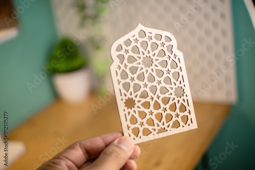 Elegant wooden Islamic geometric star pattern ornament on a wooden desk, blurred background with plant, perfect for Ramadan and Eid decoration