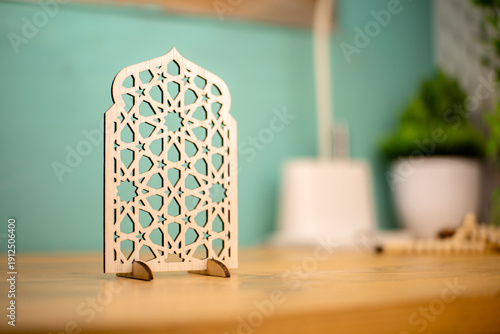 Elegant wooden Islamic geometric star pattern ornament on a wooden desk, blurred background with plant, perfect for Ramadan and Eid decoration