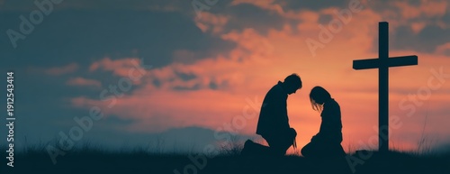 Man and woman praying together at sunset by cross  