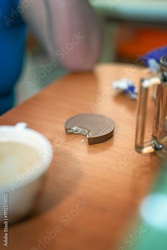 Wallpaper Mural Bitten round waffle cookie covered in milk chocolate on a table among cups and other items. Casual snack moment. Torontodigital.ca