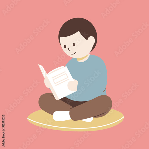 Young boy sitting cross-legged on a cushion, happily reading a book.