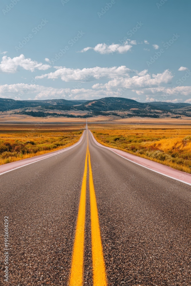 Obraz premium Long empty highway stretching through the autumn countryside into a distant horizon for road trip travel marketing background with copy space under a blue sky