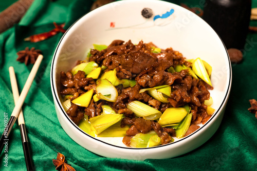 Konstfotografi Inside a restaurant, a bowl of stir-fried beef and scallions sits on a green surface
