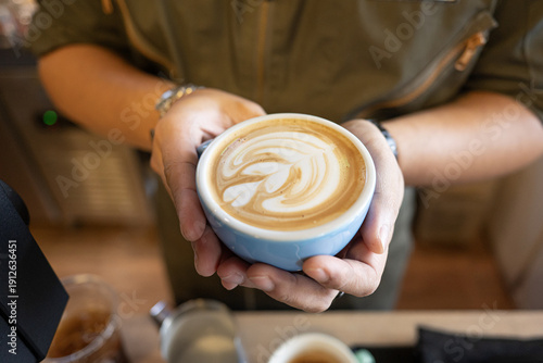 Barista latte coffee foam cafe cup milk art hand blue with elegant design held over counter, warm aroma floating, creamy surface swirling, cozy indoor scene showing care and calm morning pleasure
