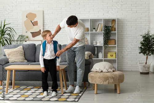Father adjusting his little son's backpack at home