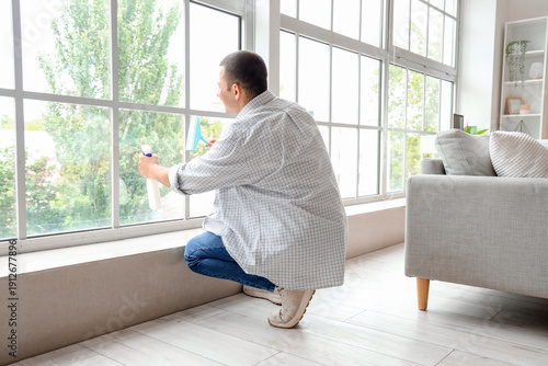 Young man cleaning window with squeegee at home, back view