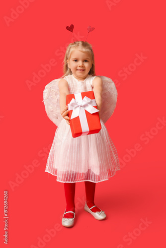 Cute little girl dressed as cupid with gift box on red background. Valentine's Day celebration