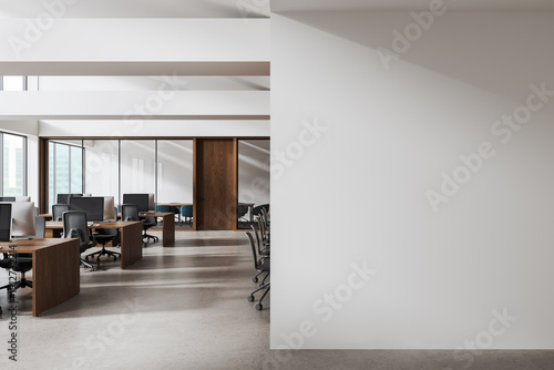 Modern office workspace with wooden desks and chairs beside large empty white wall for interior design mockup or poster template concept. 3D Rendering