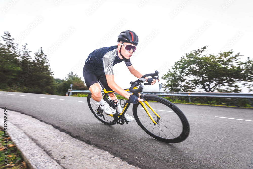 Obraz premium Young caucasian man going downhill on a corner with a road bike on an asphalt road of a mountain.