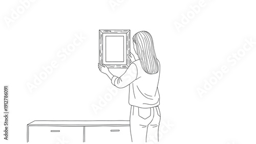 Woman hanging picture frame on wall in minimalist home setting