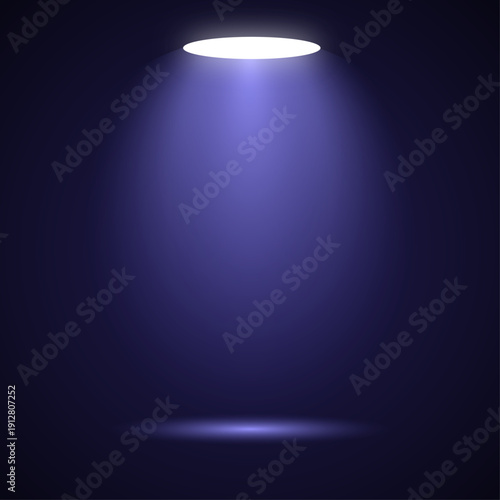 A bright spotlight shines on the black wall of an empty stage to create a glowing illuminated backdrop in the dark interior space