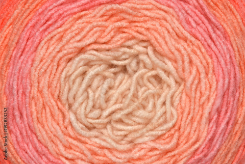 Macro shot of a soft yarn ball showing a smooth color gradient from cream to pink and orange in a circular pattern