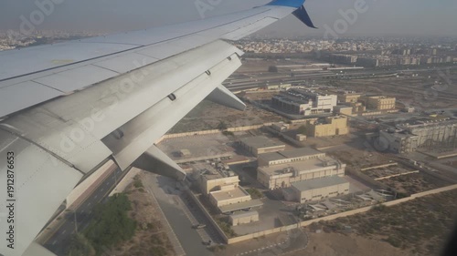 Abu Dhabi, UAE - January 18, 2026: Airplane wing with flaps extended approaches a cityscape, transitioning from descent to landing on a runway, with urban structures and ground markings visible in the
