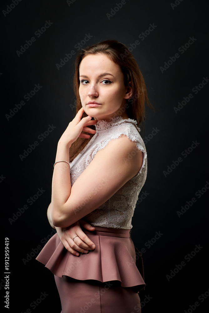 Obraz premium A woman in a pink skirt and a white lace top stands in a dark studio.