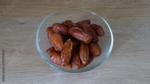Horizontal image of fresh dates in a glass bowl on a wooden surface, showcasing their rich color and texture. Perfect for healthy eating, natural foods, and Middle Eastern cuisine.