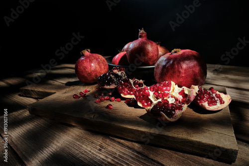 A beautiful food photography scene featuring whole pomegranates and open fruit with glistening seeds on a wooden surface, decorated by natural patterned shadows and warm sunlight