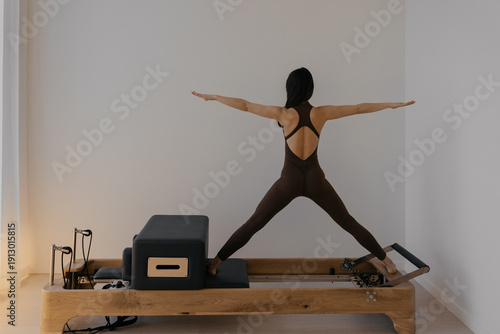 Pilates Reformer machine with Pilates box attachment in use by a slim athletic model. She performs controlled exercises on the apparatus, demonstrating effective training.