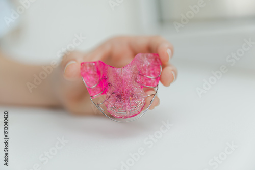 Close up of pink removable orthodontic dental plate held by fingers, pediatric dentistry and tooth alignment correction device concept