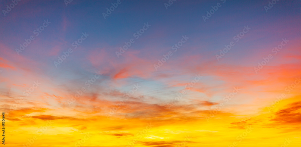 Fototapeta premium Vibrant sunset sky with dramatic orange and purple clouds,A breathtaking sunset sky featuring a beautiful gradient of deep purple, fiery orange, and golden yellow. The wispy cirrus clouds 