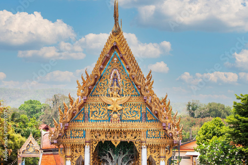 Fotografie Traditional Thai temple roof with colorful tiles and golden decorative gables against blue sky