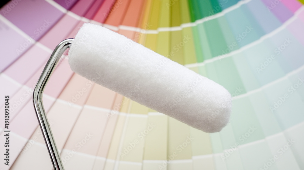 Obraz premium Paint roller ready for use, placed against a fanned-out color palette, representing renovation and interior design choices