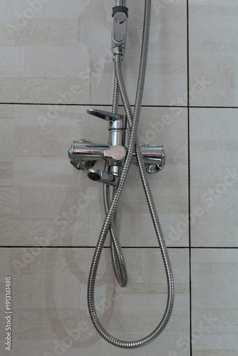 A chrome shower faucet mounted on a tiled wall. Selective focus. Shallow depth of field.