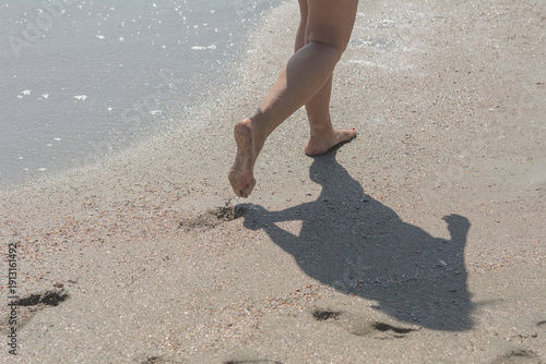 A close-up of a woman's bare feet with a red manicure walking along the sea sand on a bright, sunny autumn day. Selective focus