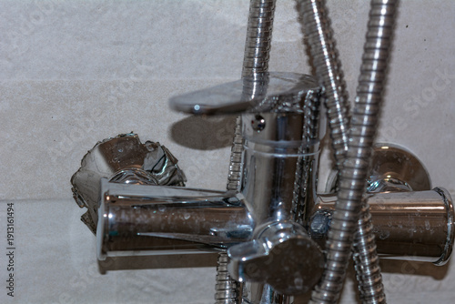Damaged wall mount on a chrome shower faucet installed on a tiled wall. Selective focus. Shallow depth of field