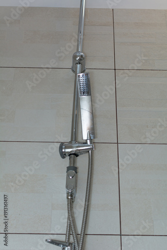 A chrome shower faucet mounted on a tiled wall. Selective focus. Shallow depth of field.