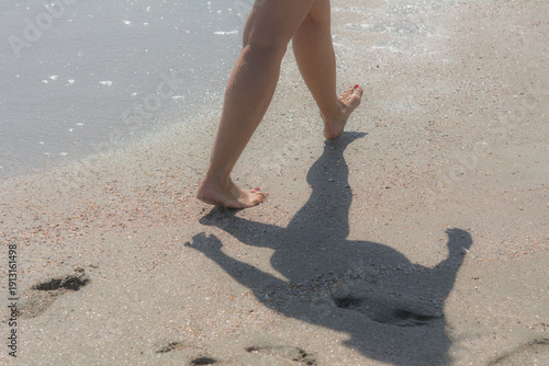 A close-up of a woman's bare feet with a red manicure walking along the sea sand on a bright, sunny autumn day. Selective focus