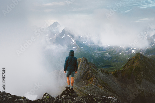 Man tourist travel in Norway solo standing on cliff climbing foggy mountains in Lofoten islands, extreme adventure traveler hiking tour summer vacation outdoor freedom exploration wanderlust getaway