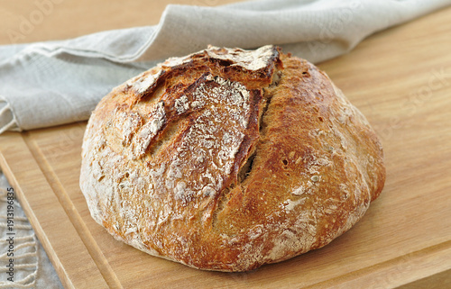 Round sourdough bread loaf, with a crispy crust, dusted with flour, resting on a rustic linen cloth on a wooden surface. Home bakery, traditional baking concept. Realistic image, Negative space