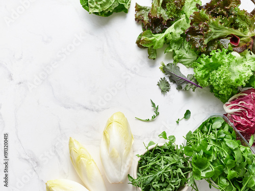Variety of lettuces and vegetables on marble countertop for healthy meal preparation and salad making in the kitchen