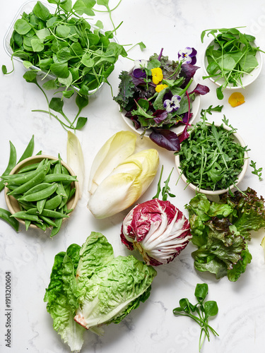 Variety of lettuces and vegetables on marble countertop for healthy meal preparation in modern kitchen