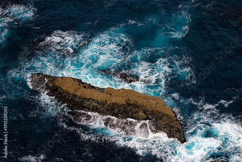 Aerial Ocean Waves Crashing Over Rugged Rock Outcrop