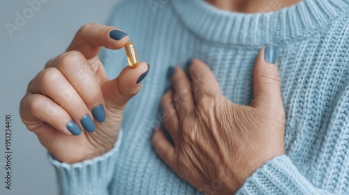 Close up of senior woman holding vitamin capsule with hand on chest in cozy blue sweater